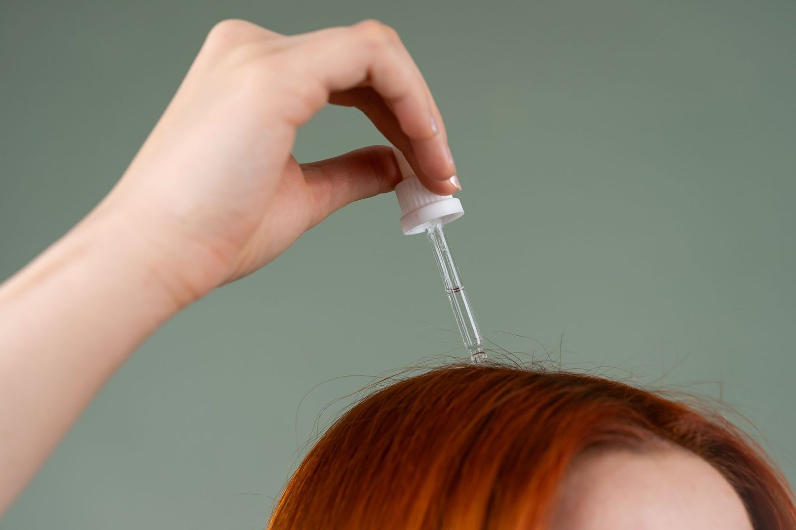 Hand droppar vätska från pipett på en persons hårbotten
